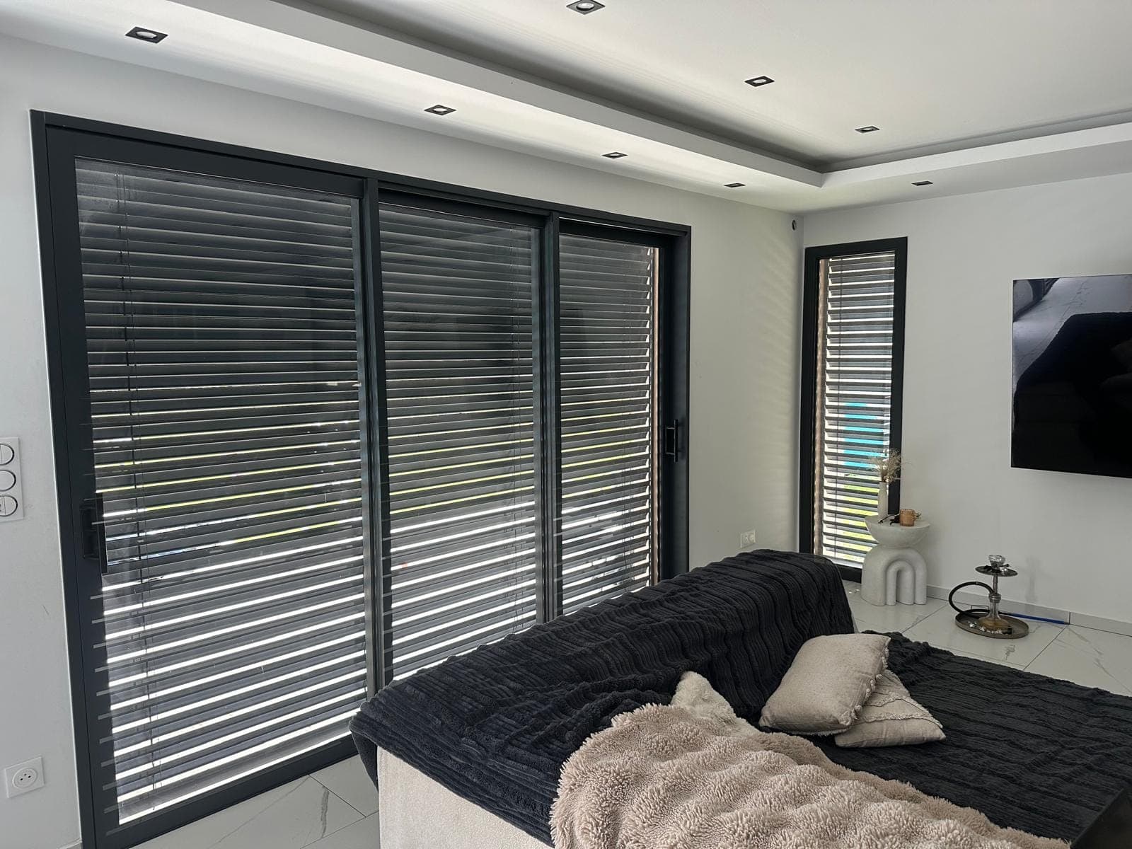 Brise-soleil orientables en aluminium sur les baies vitrées d'une chambre, posés par REM Fermetures